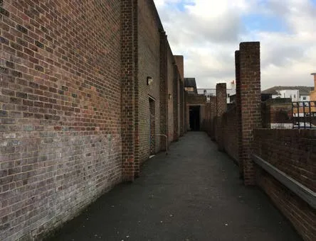 The old alleyway: a narrow tarmac path between tall brick walls, with a dark doorway at the far end