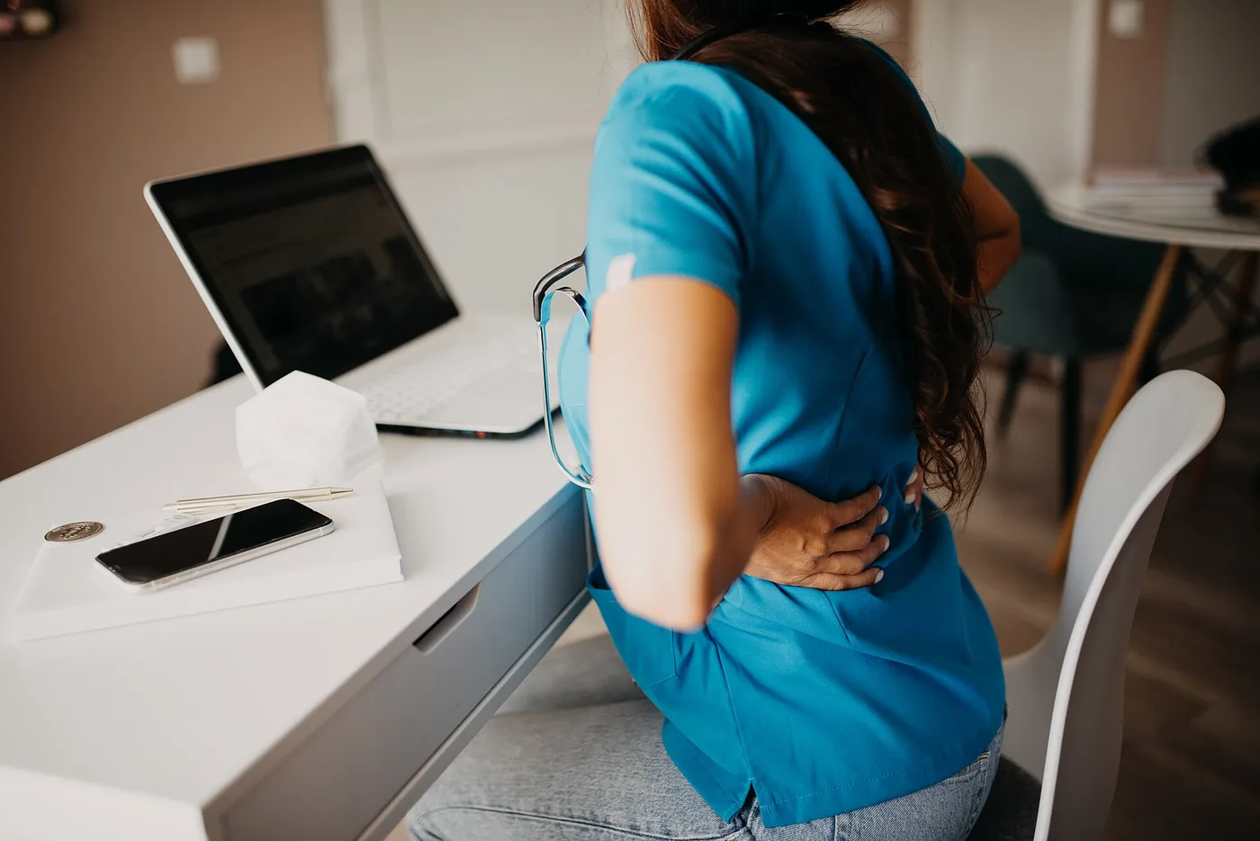 A person at a desk in a home office holding their lower back