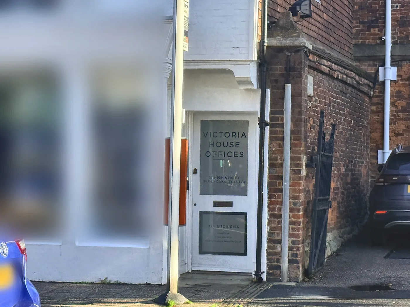 The white front door of Victoria House Offices on High Street, Sevenoaks, beside a brick wall and an iron gate