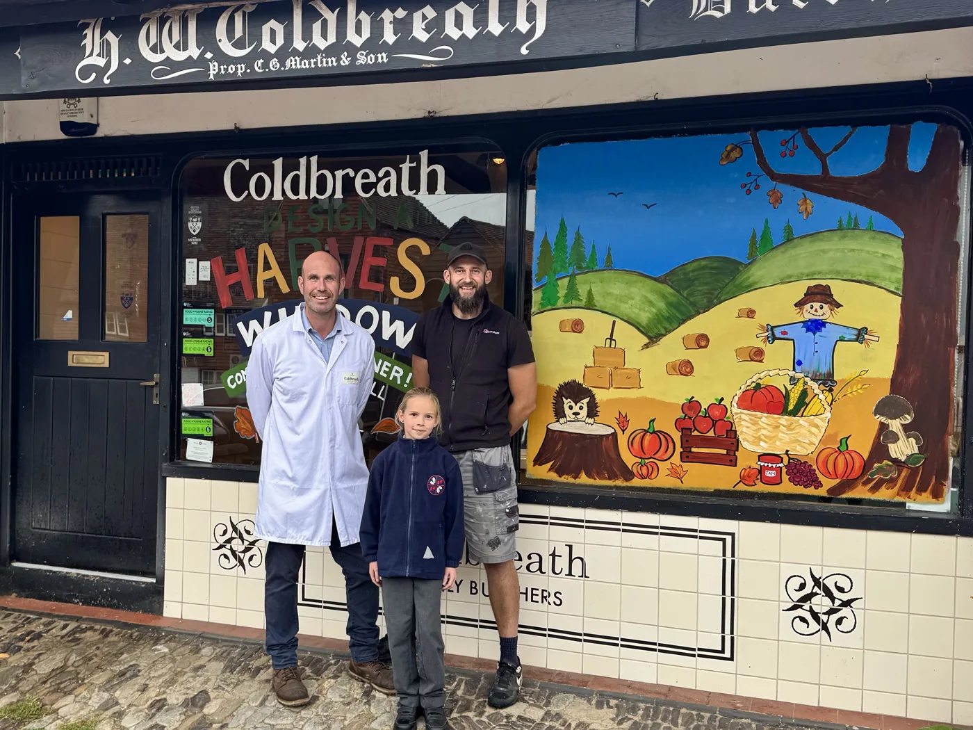 Elsie Blundell with Robert Martin, owner of Coldbreath Butchers, and artist Paul Spiers outside the shop and its painted harvest window
