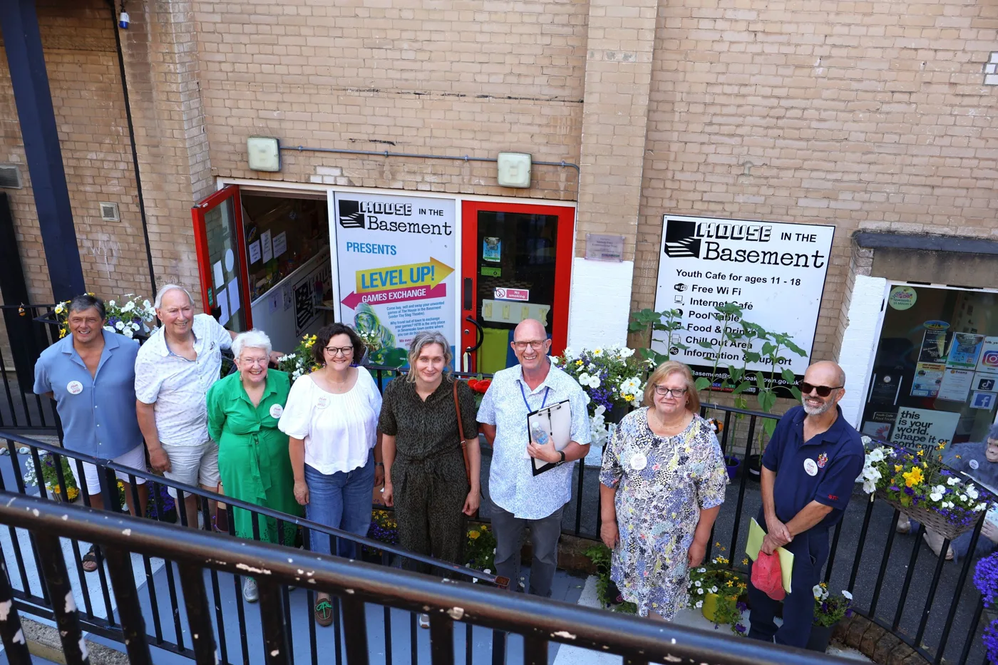 A group of judges, council staff and councillors standing outside the House in the Basement youth café, with flower planters along the railings