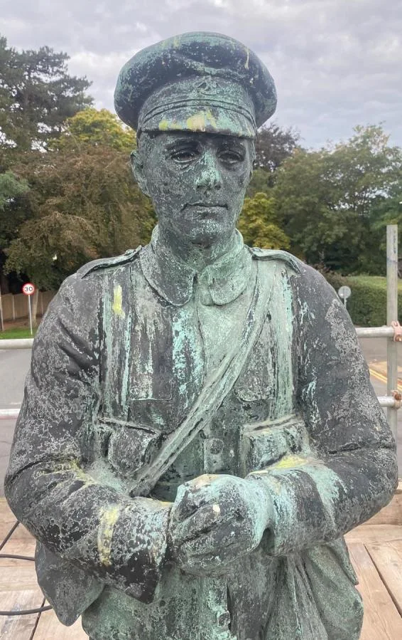 The bronze soldier on the Vine War Memorial before treatment, streaked with pale green corrosion and yellow marks, with scaffolding behind