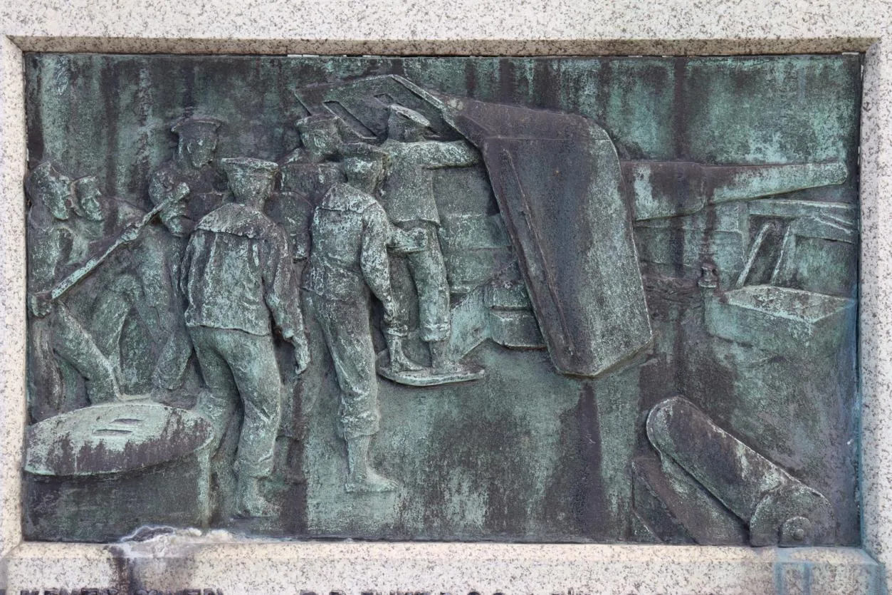 Bronze relief panel of sailors loading a ship's gun, before treatment, almost entirely covered in pale green and dark streaked corrosion