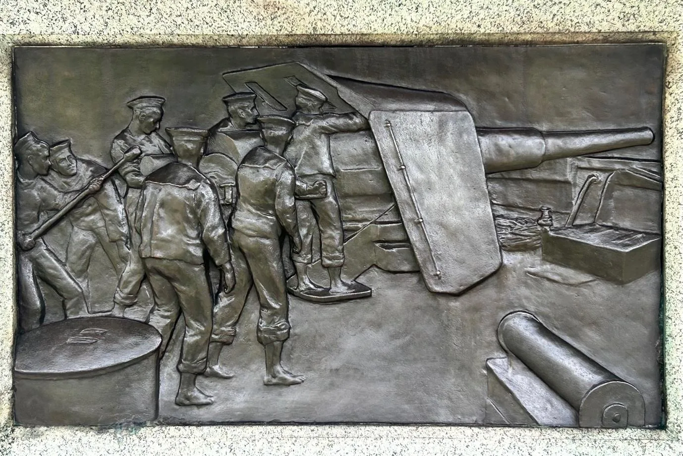 The same relief panel after treatment, an even dark bronze in which each sailor, the gun barrel and the shield stand out
